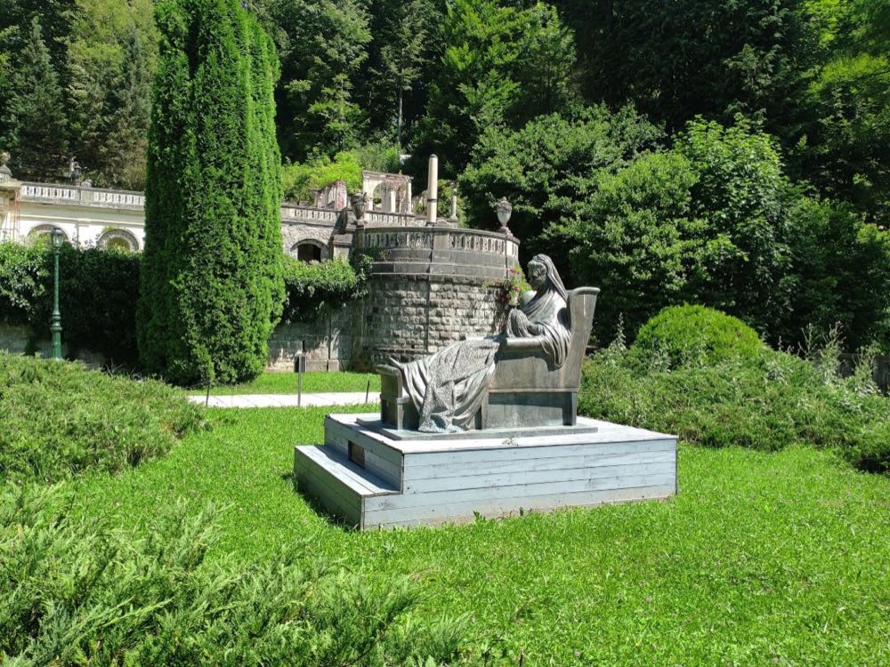Statuen av dronning Elisabeth, sittende i en lenestol, på en sokkel av tre i parken ved Peleș-slottet