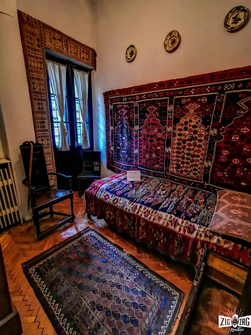 Chambre de la Vila Luminiș, avec kilims et tapis tissés colorés aux murs et sur le lit, vieilles chaises en bois et fenêtre à rideaux